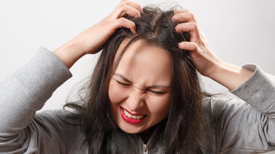 Pregnant woman looking at her scalp in a mirror, concerned about dandruff.