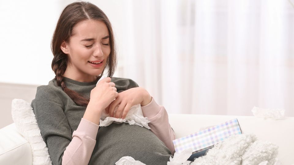 Pregnant woman sitting on a sofa, looking emotional.