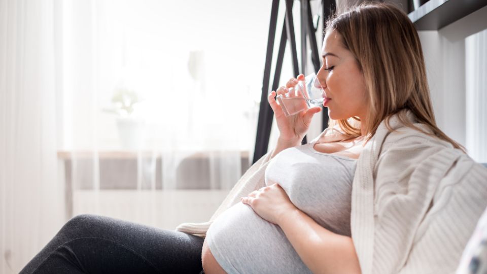 A pregnant woman drinking a glass of water, looking refreshed and hydrated.