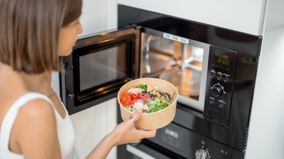 A pregnant woman using a microwave in the kitchen, with a focus on her carefully handling food.