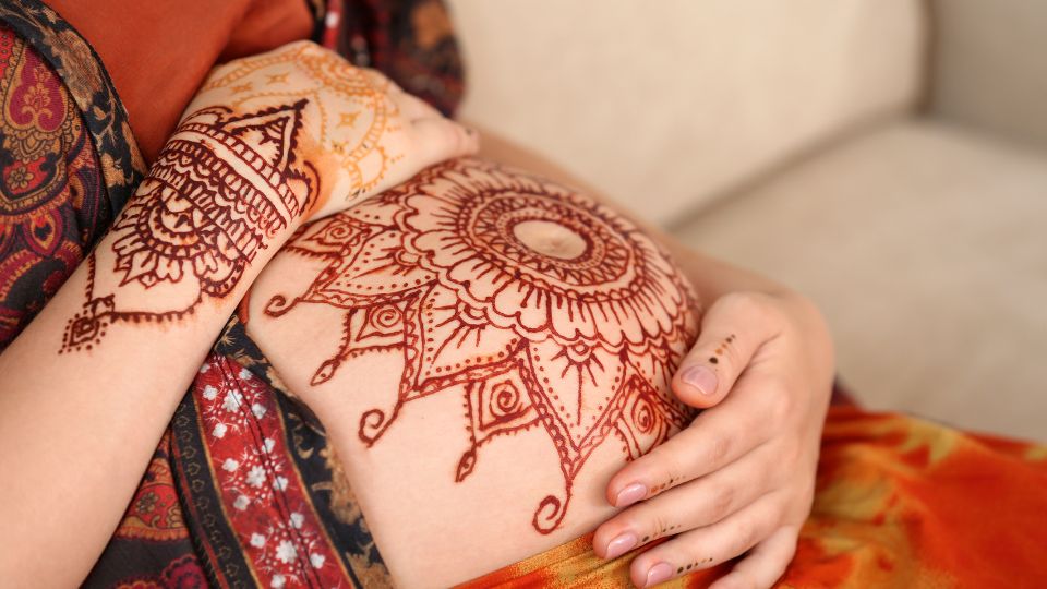 A pregnant woman having henna applied to her hands by a professional.