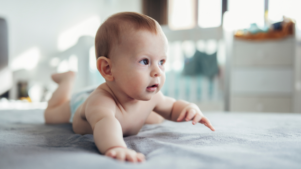 A baby learning to crawl on a soft play mat with supportive toys around.